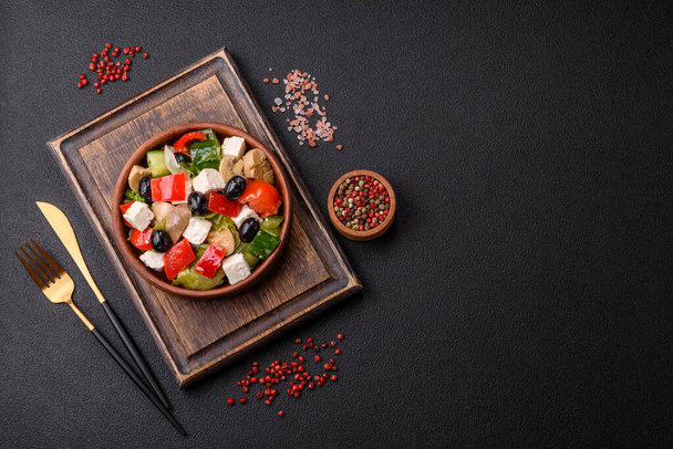 Delicious fresh juicy salad of sweet peppers, cheese, olives, tomatoes, cucumbers with salt and spices on a dark concrete background - Photo, Image