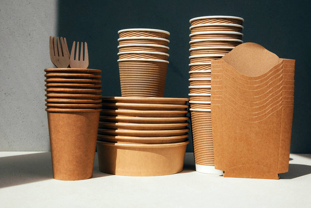 Набор бумажной посуды и деревянных столовых приборов на сером фоне. Экологически чистые, нулевые отходы. Вид спереди - Фото, изображение