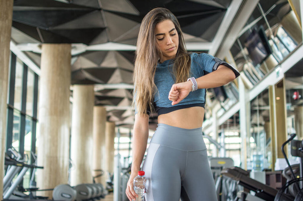 Młoda sportowiec sprawdza swoją aktywność fizyczną i spalonych kalorii na smartwatch po treningu w siłowni - Zdjęcie, obraz