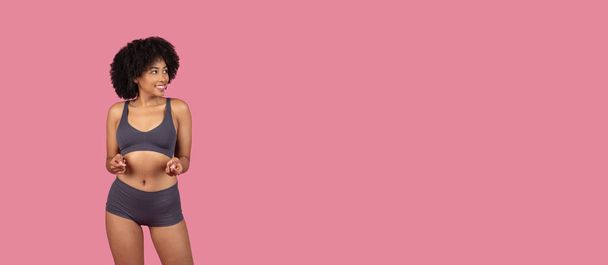 Játékos fiatal fekete nő sport öltözékben gesztikulál maga felé egy rózsaszín háttér - Fotó, kép