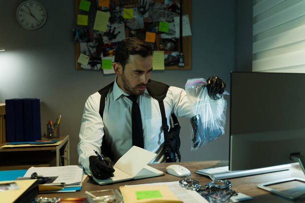 Частный детектив тщательно анализирует пистолет как улику в небольшом офисе, фиксируя напряжение в процессе раскрытия преступления - Фото, изображение