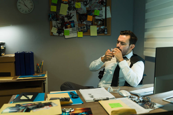 Kriminalbeamter macht Pause von der Arbeit an einem Kriminalfall und raucht nachts in seinem Büro eine Zigarette - Foto, Bild