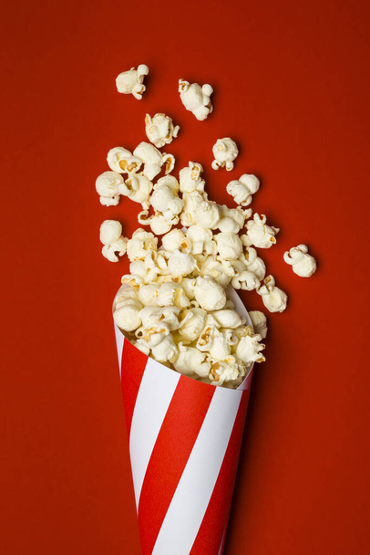 Flat lay composition with popcorn in paper cone on red background. - Photo, Image