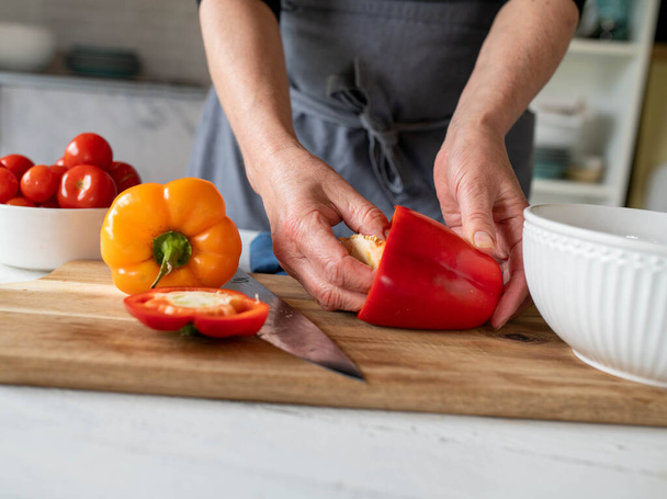 Esvazie um pimentão vermelho pela mão das mulheres em uma placa de corte na cozinha - Foto, Imagem