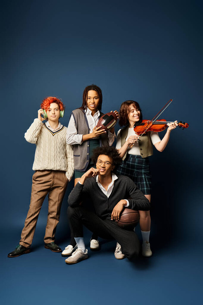 Diverse young friends, including a nonbinary person, in stylish attire, standing united with musical instruments against a dark blue background. - Photo, Image