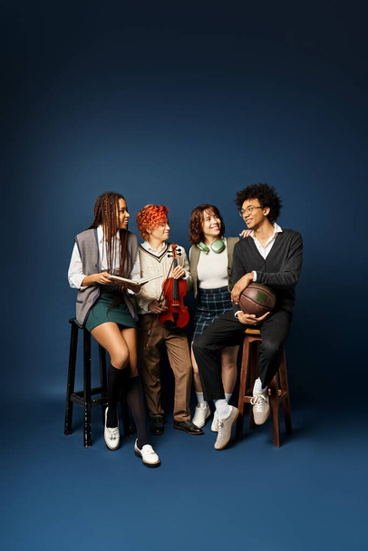 Eine Gruppe junger multikultureller Freunde, darunter eine nichtbinäre Person, die eng nebeneinander in stilvoller Kleidung vor dunkelblauem Hintergrund sitzt. - Foto, Bild