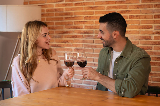  Ζευγάρι τσούζει ποτήρια κόκκινο κρασί ενώ έχει ένα ρομαντικό ραντεβού στο εστιατόριο, γιορτάζοντας την ημέρα του Αγίου Βαλεντίνου. Κοντινό πλάνο των ανδρών και των γυναικών χέρια των εραστών αυξάνεται για μια εορταστική πρόποση - Φωτογραφία, εικόνα