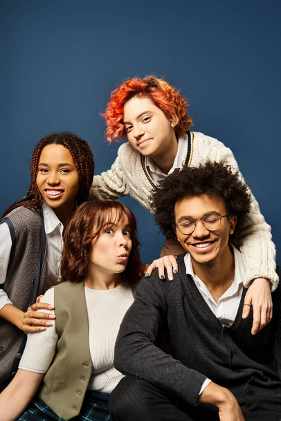 Junge multikulturelle Freunde sitzen nebeneinander in stylischer Kleidung auf dunkelblauem Hintergrund. - Foto, Bild