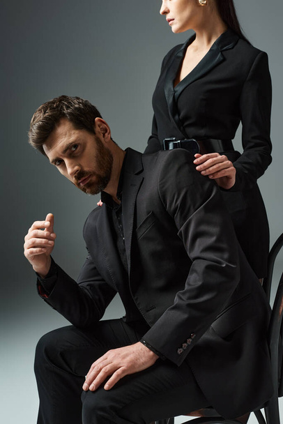 A man and a woman in elegant attire pose near a chair together. - Photo, Image