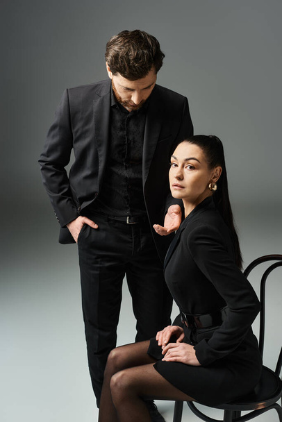 Чоловік стоїть поруч з жінкою в чорній сукні, обидва виглядають елегантно і захоплююче. - Фото, зображення