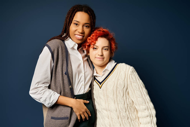Zwei junge multikulturelle Freunde, darunter eine nicht binäre Person, stehen vereint in stilvoller Kleidung vor dunkelblauem Hintergrund. - Foto, Bild