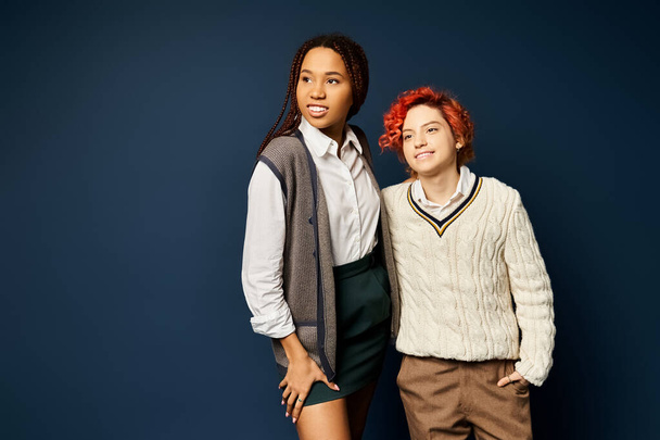 a woman, along with a nonbinary individual, stand together in stylish attire against a dark blue background. - Photo, Image