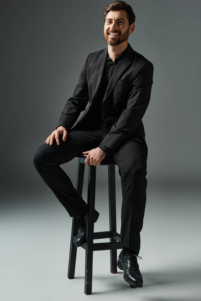 A distinguished man in a suit gracefully sits on a stool. - Photo, Image