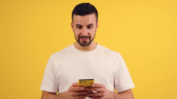 Портрет счастливого человека с помощью мобильного телефона, смс-ки на желтом фоне, смотрящего в камеру. Понятие человеческих эмоций, выражение лица. Пространство для копирования рекламы - Кадры, видео