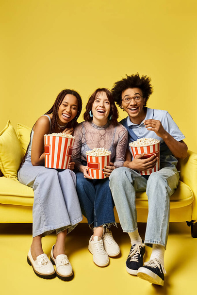 Junge multikulturelle Freunde sitzen auf einer Couch, halten Popcornboxen in der Hand und genießen gemeinsam einen Filmabend in einem stilvollen Studio-Ambiente. - Foto, Bild