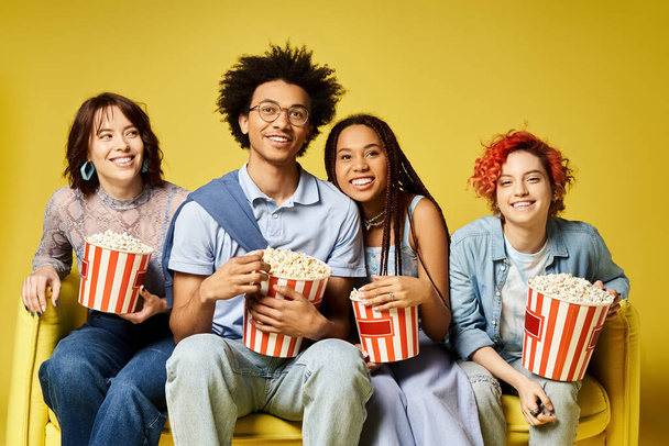 Eine bunte Gruppe von Menschen sitzt zusammen und hält Eimer mit Popcorn in einer modischen Studiokulisse. - Foto, Bild