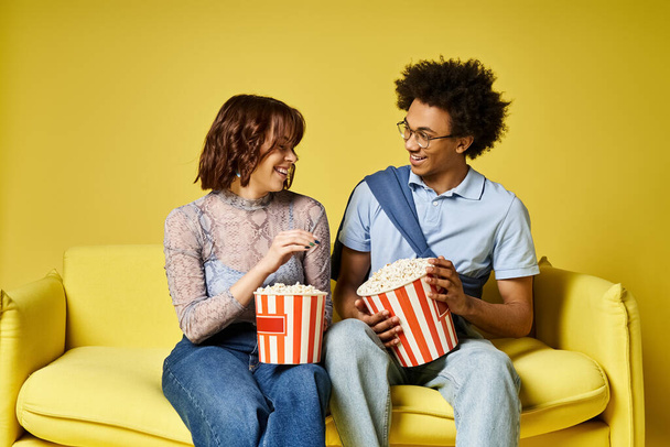 Muž a žena mají rádi popcorn, zatímco sedí na útulném gauči. - Fotografie, Obrázek