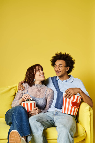 Mies ja nainen tyylikkäässä puvussa rentoutuvat keltaisella sohvalla nauttien hetken rauhasta ja yhdessäolosta valoisassa studiossa.. - Valokuva, kuva