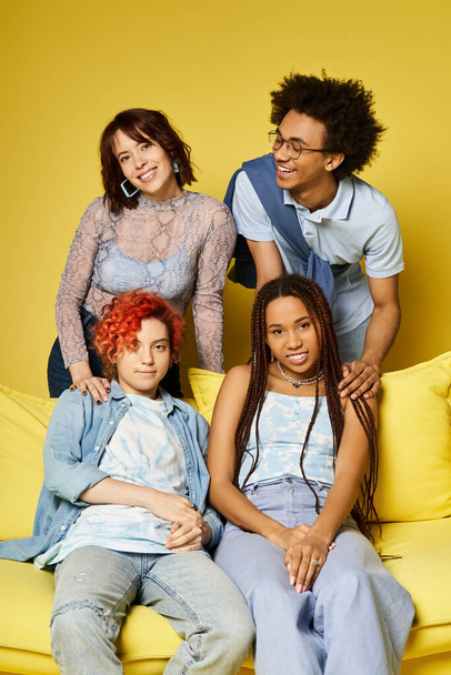 Multicultural friends in stylish attire sit atop a vibrant yellow couch in a cozy studio setting, creating a warm and inclusive atmosphere. - Photo, Image