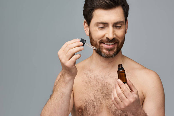 Shirtless man applying serum on his face. - Photo, Image