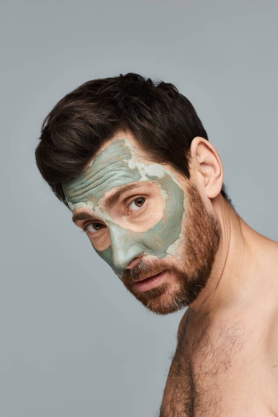 Ένας άντρας φοράει μάσκα προσώπου, εστιάζοντας στη ρουτίνα φροντίδας του δέρματος.. - Φωτογραφία, εικόνα