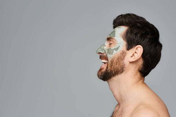 Hemdloser Mann zeigt Gesichtsmaske und umarmt seine Hautpflege-Routine. - Foto, Bild