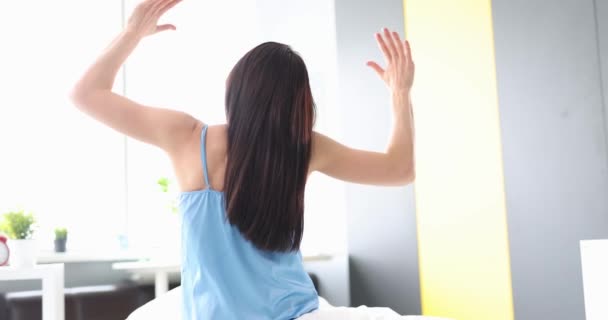 Mujer joven levanta las manos mientras está sentada en la cama. Inicie el concepto de día positivo - Imágenes, Vídeo
