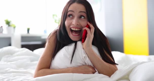 Mosolygó boldog nő beszél telefonon, miközben fekszik az ágyban. Pozitív beszélgetés telefonon - Felvétel, videó