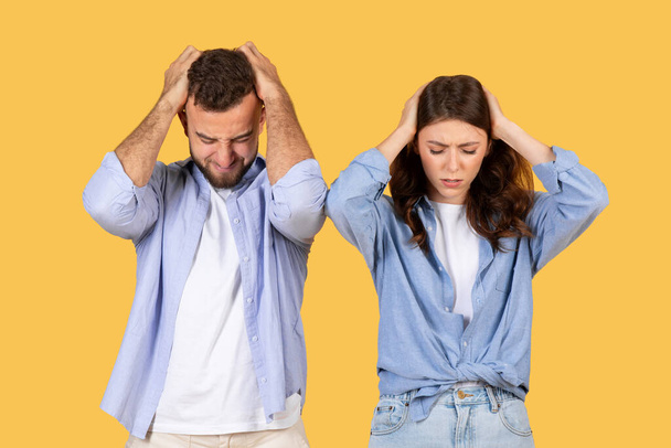 Two adults express frustration with hands on their heads against a yellow background - Photo, Image