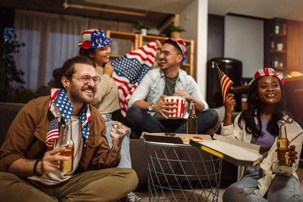 Freunde verschiedener Rassen beobachten den Sport zu Hause mit amerikanischen Flaggen. - Foto, Bild
