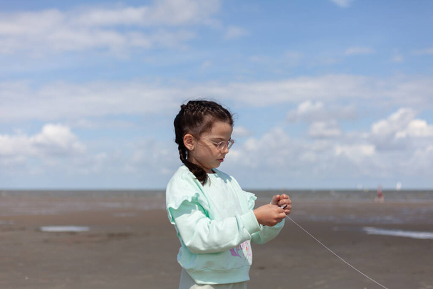 Little girl in clothes stands with a kite string on the beach - Photo, Image