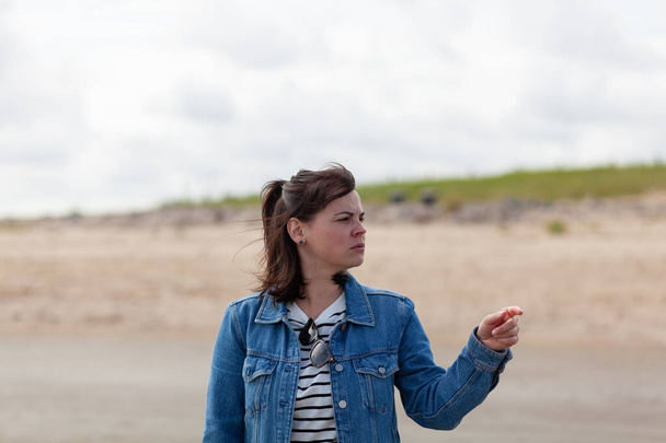 Cute girl in a denim jacket stands and looks into the distance on the beach - Photo, Image