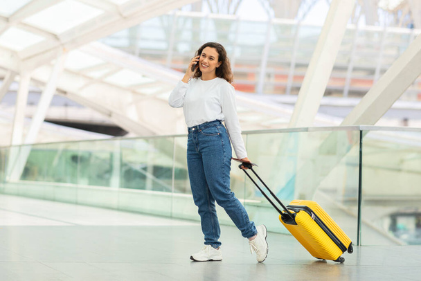 Occupato viaggiatore donna con valigia impegnarsi in una conversazione telefonica durante il ritmo attraverso l'aeroporto - Foto, immagini