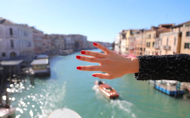 Mano de mujer joven con dedos delgados y uñas rojas y Gran Canal de Venecia con barcos en el fondo - Foto, Imagen