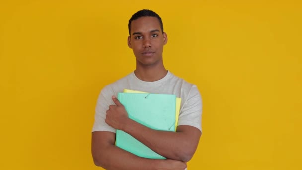Fiducioso ritratto di ragazzo studente sorridente in possesso di cartella di file accademici su sfondo giallo studio. Istruzione stile di vita concetto. - Filmati, video