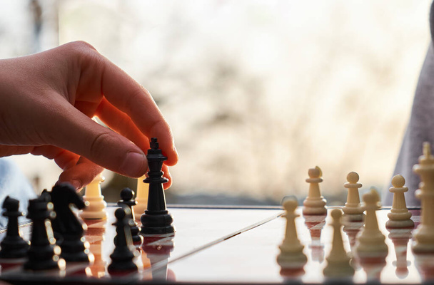 Шахматная доска деревянная. Человек, играющий в шахматы на природе. Человек держит в руках черного короля.. - Фото, изображение