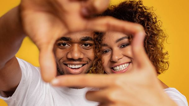 Afro-américain homme et femme riant et montrant panneau de cadre avec leurs mains sur fond orange
 - Photo, image