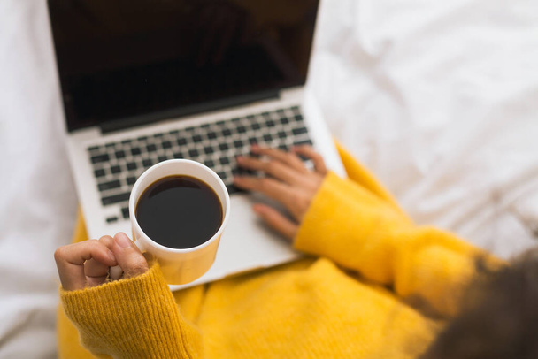 Femme surfant sur Internet sur ordinateur portable et buvant du café au lit - Photo, image