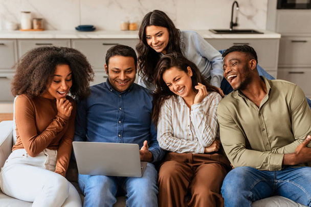 Des amis multiraciaux proches partagent avec enthousiasme du contenu sur un ordinateur portable, affichant plaisir et intérêt collectifs - Photo, image