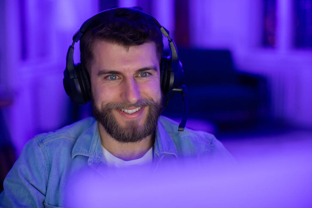 Hombre contento gamer con una sonrisa jugando juegos por la noche con iluminación de fondo púrpura vibrante, primer plano - Foto, imagen