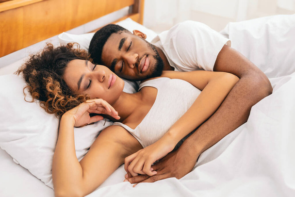 Έντονη ματιά του Αφροαμερικανού ζευγαριού που μοιράζεται μια τρυφερή αγκαλιά στο κρεβάτι του, απεικονίζοντας την ουσία της αγάπης και της συνεργασίας - Φωτογραφία, εικόνα