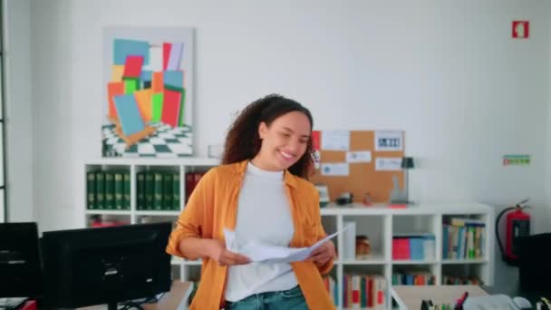 Vrolijke Spaanse of Braziliaanse jonge vrouw, kantoormedewerker, dansend vrolijk in een modern kantoor, kreeg een promotie, sloot een goede deal, verheugt zich aan het einde van de werkdag, gooit documenten, glimlach - Video
