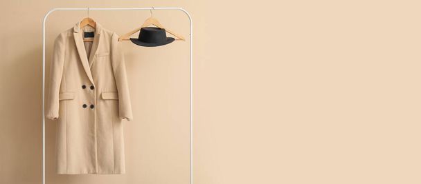 Stylish coat and hat hanging on rack against beige wall. Banner for design - Photo, Image