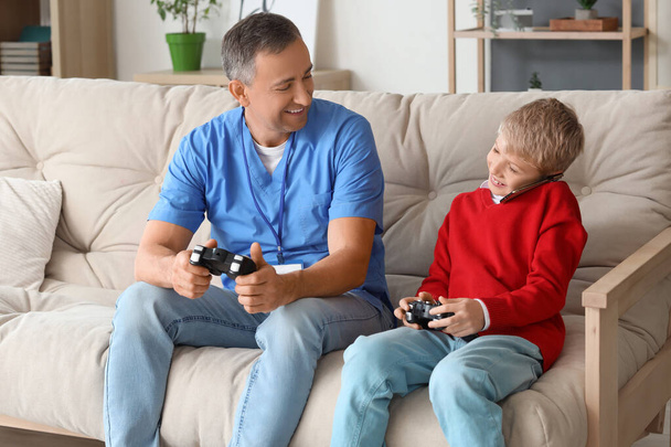自宅で携帯電話で話すゲームパッドを持つ成熟した医師と彼の息子 - 写真・画像