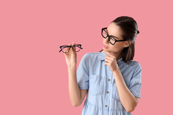 Mujer joven reflexiva con anteojos sobre fondo rosa - Foto, Imagen
