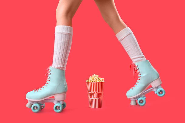 Ведро попкорна и ноги женщины в роликовых коньках на красном фоне - Фото, изображение