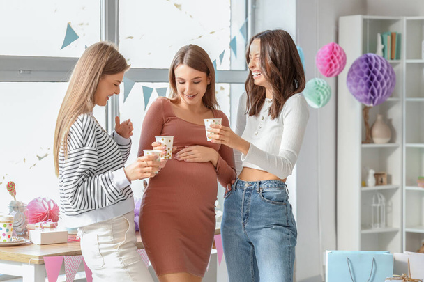 Молодая беременная женщина с друзьями, пьющими на вечеринке в честь рождения ребенка - Фото, изображение