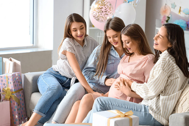 Female friends touching belly of young pregnant woman at baby shower party - Photo, Image