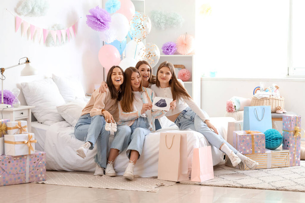 Junge schwangere Frau mit Sonogramm-Bild und ihre Freunde bei Babyduschparty im Schlafzimmer - Foto, Bild