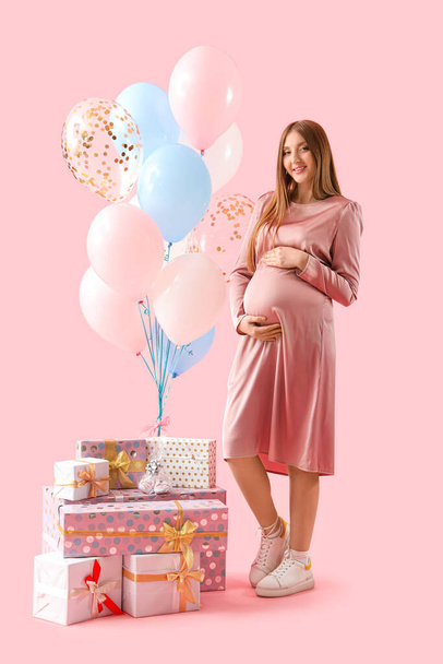 Mujer embarazada joven con regalos de ducha de bebé y globos sobre fondo rosa - Foto, Imagen